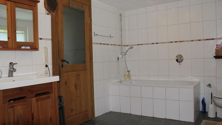 Ein geräumiges Badezimmer mit weiß gefliesten Wänden und einem Holztür. Es gibt eine Badewanne, eine Dusche und ein Doppelwaschbecken.