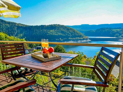 Ein schöner Ausblick auf einen See mit grünen Hügeln. Ein Tisch mit zwei Gläsern und einem Obstkorb steht auf der Terrasse.