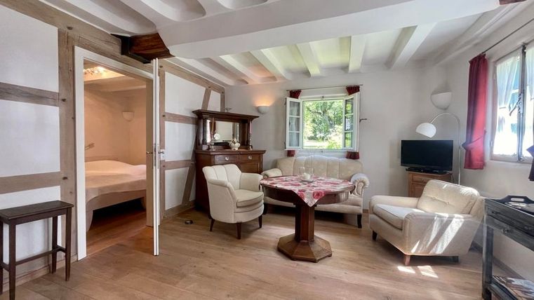 Ein gemütliches Wohnzimmer mit Holzvertäfelung und hellem Mobiliar. Das Zimmer hat große Fenster, die viel Tageslicht hereinlassen.