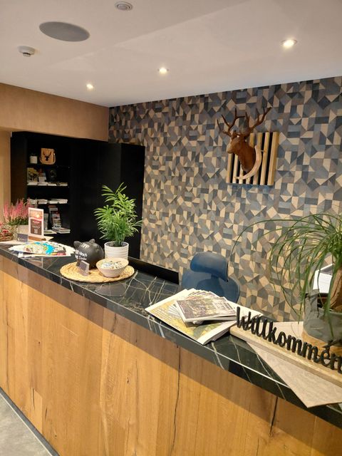 Ein moderner Empfangsbereich mit einer Holztheke und stilvollen Dekorationen. An der Wand sind geometrische Muster und ein Tierkopf angebracht.