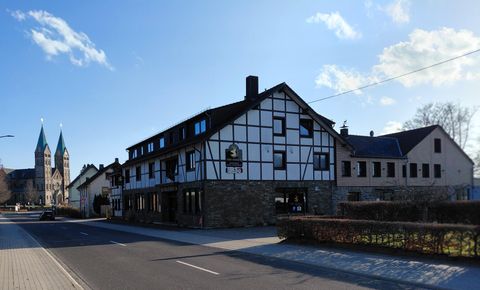 A charming half-timbered house with a street café. In the background, two pointed church towers are visible.