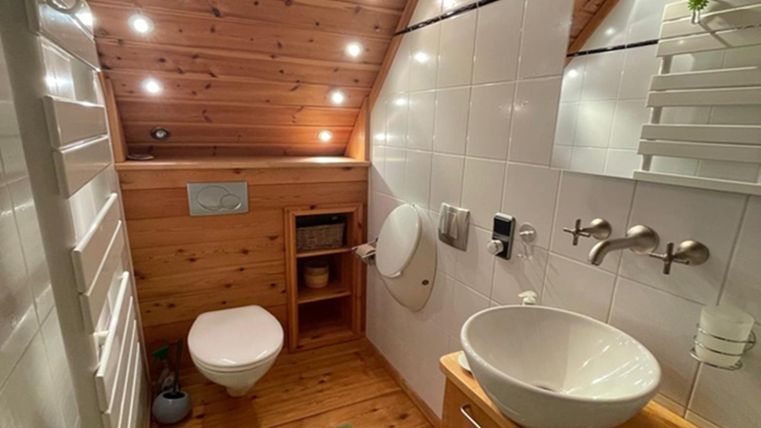 Een moderne badkamer met houten plafond en lichte tegels. Het beschikt over een toilet, een wastafel en een aangename verlichting.