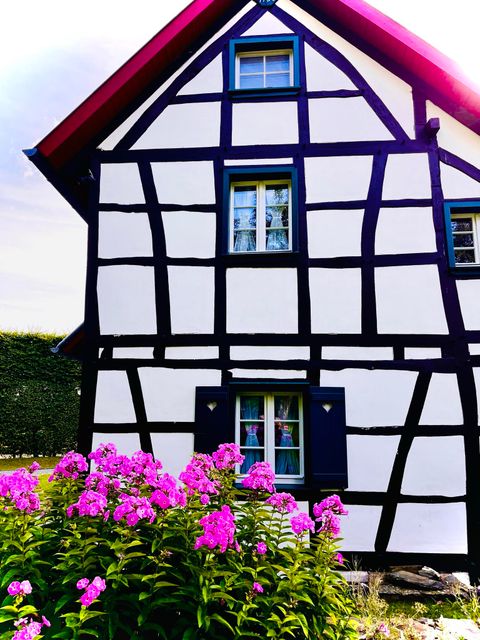 Een traditioneel vakwerkhuis met witte muren en zwarte balken. Voor het huis bloeien kleurrijke bloemen.