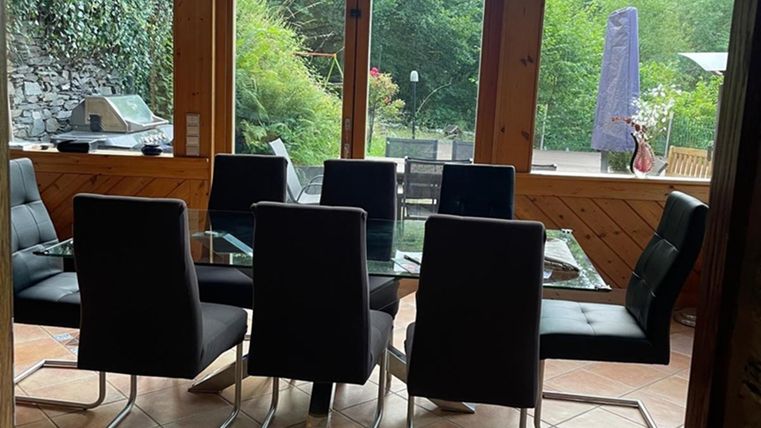Een moderne eetruimte met een glazen tafel en zwarte stoelen. Grote ramen bieden uitzicht op de groene omgeving.