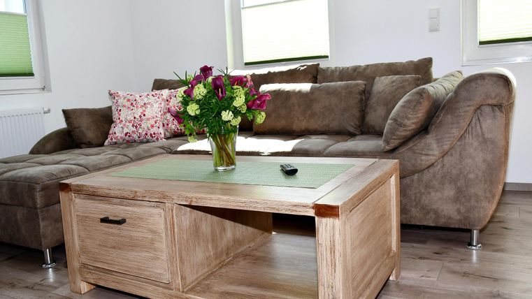 Un salon douillet avec un canapé marron et une table en bois. Sur la table se trouve un bouquet de fleurs dans un vase.