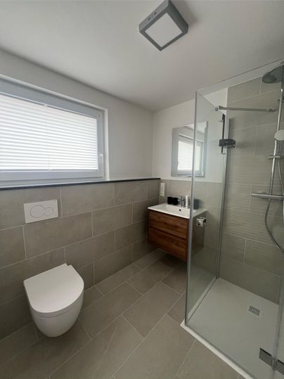 Een moderne badkamer met een glazen douche en een stijlvolle wastafel. De muren zijn in neutrale kleuren gehouden, en er is een raam voor daglicht.