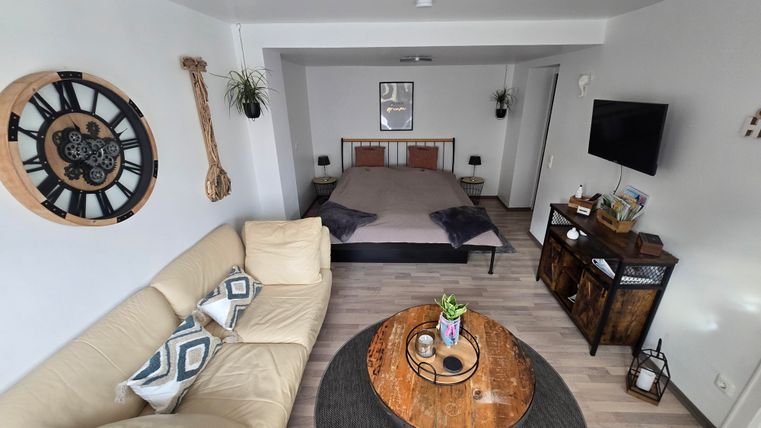 Ein modernes Zimmer mit einem bequemen Sofa und einem großen Bett. An der Wand hängen dekorative Elemente, und ein runder Teppich liegt auf dem Boden.