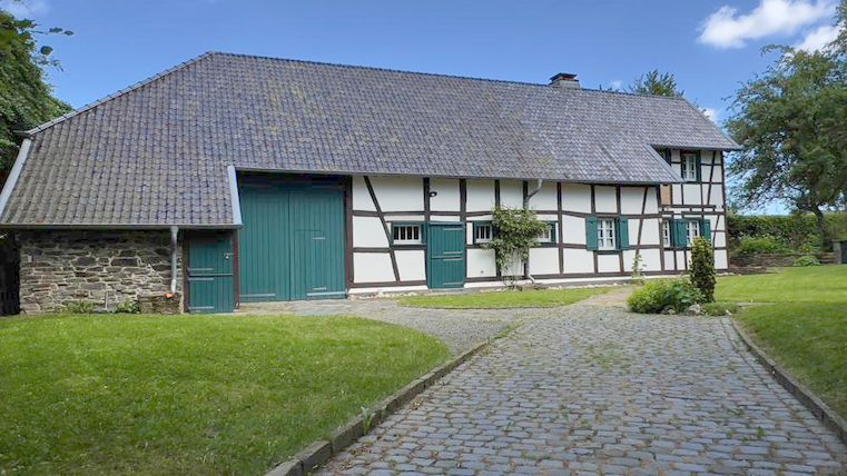 Ein reizendes Fachwerkhaus mit einem gepflasterten Weg und einer grünen Wiese. Der Himmel ist klar und blau.