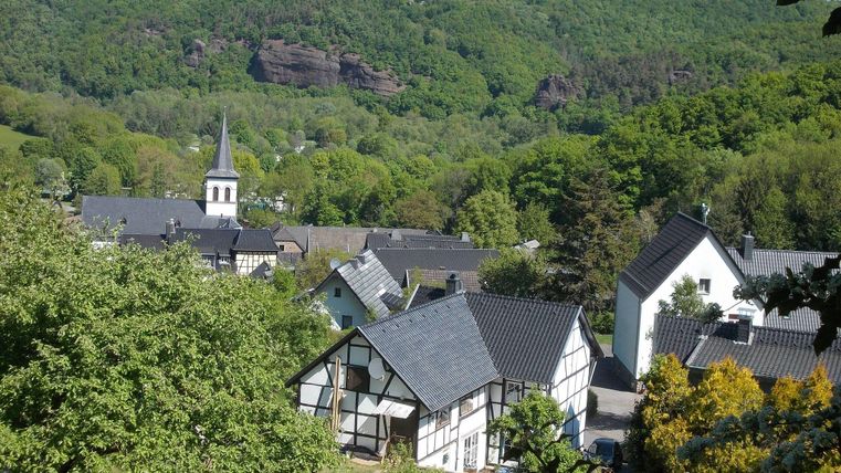 Eine malerische Dorfansicht mit traditionellen Gebäuden und einer Kirche. Umgeben von üppigem Grün und sanften Hügeln.
