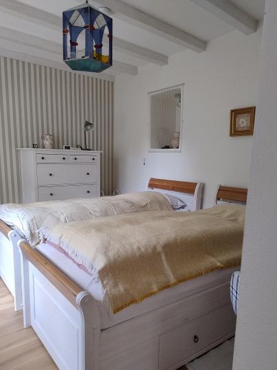 A cozy bedroom with two beds and a bright wall design. A colorful ceiling lamp and a wardrobe complete the picture.