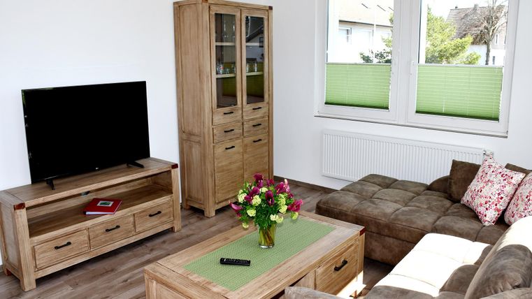 Un salon moderne avec une télévision, une élégante commode en bois et un canapé confortable. Sur la table se trouve un vase avec des fleurs colorées.