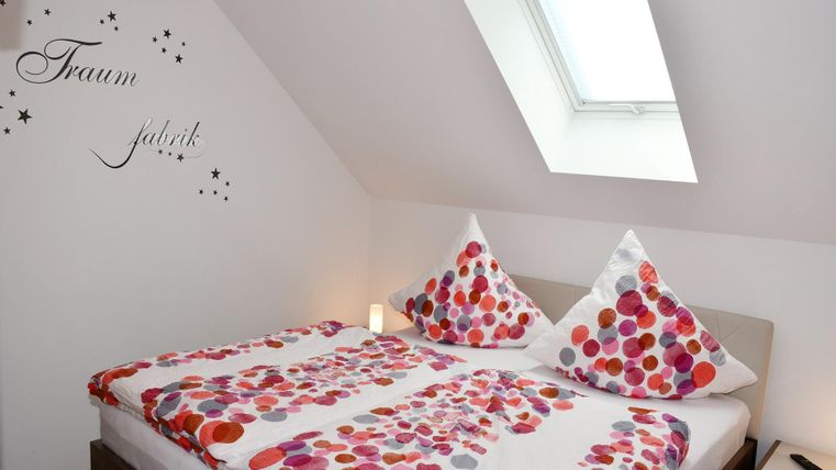 Une chambre confortable avec un lit double et des coussins colorés. Sur le mur se trouve l'inscription "Usine de rêves".