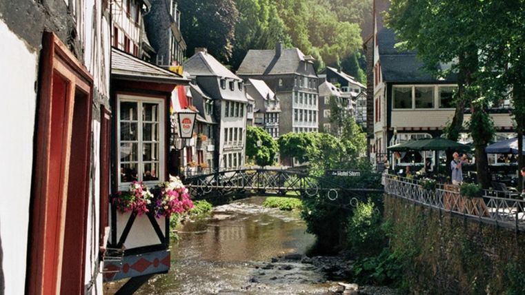 Une ville pittoresque au bord de la rivière avec des maisons historiques et des arbres. L'atmosphère est calme et accueillante.