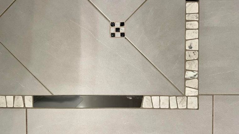 Ein modernes Fliesenmuster in Grautönen mit dekorativen Details. Die Struktur zeigt eine Kombination aus verschiedenen Fliesenformen und -farben.