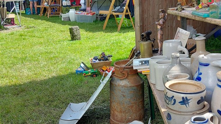 Een vlooienmarkt in de open lucht met stands vol kleding en antieke voorwerpen. Op een tafel zijn verschillende keramieken en huishoudelijke artikelen opgesteld.
