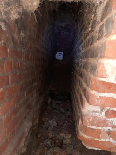 Ein schmaler, dunkel aussehender Tunnel aus Ziegelsteinen mit Steinen und Schutt am Boden. Am Ende des Tunnels ist ein schwaches Licht sichtbar.