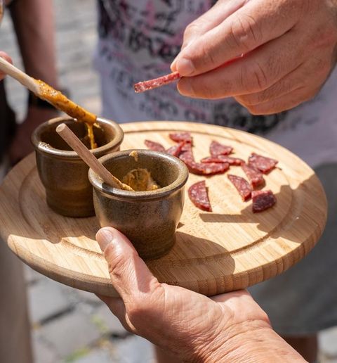 Eine ausgestreckte Hand hält ein Eis im Waffelhorn mit Sahnehaube. Im Hintergrund sind historische Fachwerkhäuser zu sehen.