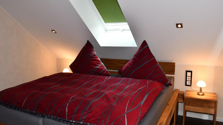 Une chambre confortable avec un grand lit double et des coussins rouges. La pièce a un velux et une lampe de chevet.