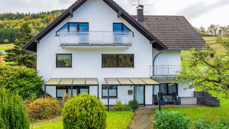 Ein modernes Haus mit einem großen Garten. Es hat Balkone und ist von Bäumen umgeben.