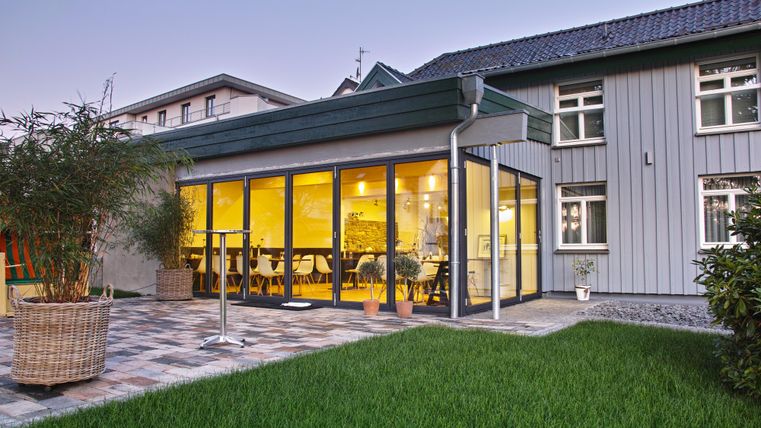 Ein moderner Anbau mit großen Fenstern und einem gemütlichen Innenraum. Der Garten ist gut gepflegt mit grünem Rasen und Pflanzen.