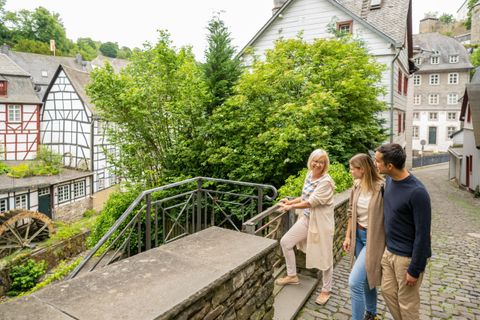 Eine Gruppe von drei Personen geht eine malerische Treppe hinunter. Im Hintergrund sind traditionelle Fachwerkhäuser und üppiges Grün zu sehen.