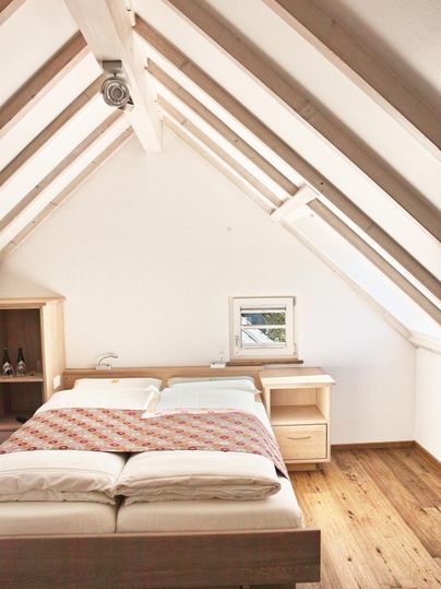 Ein gemütliches Schlafzimmer mit einem großen Bett und Holzfußboden. Die Decke hat eine moderne Dachkonstruktion mit sichtbaren Balken.