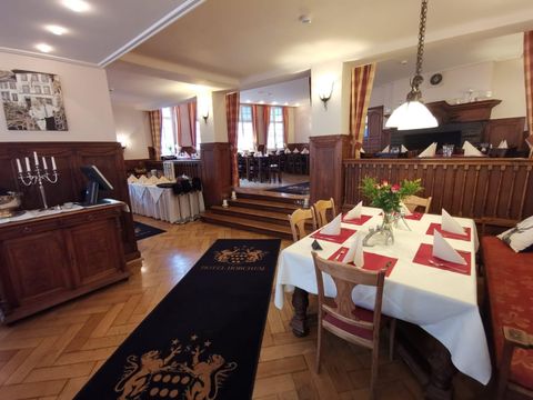 Ein elegantes Restaurant mit Holzinterieur und gedeckten Tischen. Im Hintergrund sind weitere Tische und Fenster mit Vorhängen zu sehen.