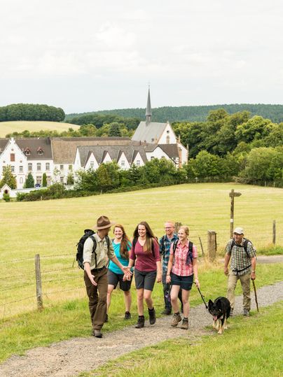 Ein Ranger führt eine Gruppe. Im Hintergrund sieht man das Kloster Mariawald.