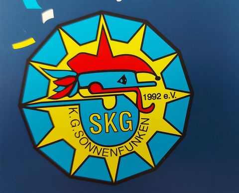 Ein bunter Vereinslogo mit einem stilisierten Fisch und einer Sonne. Der Text zeigt "K.G. SONNENFUNKEN" und die Jahreszahl 1992.
