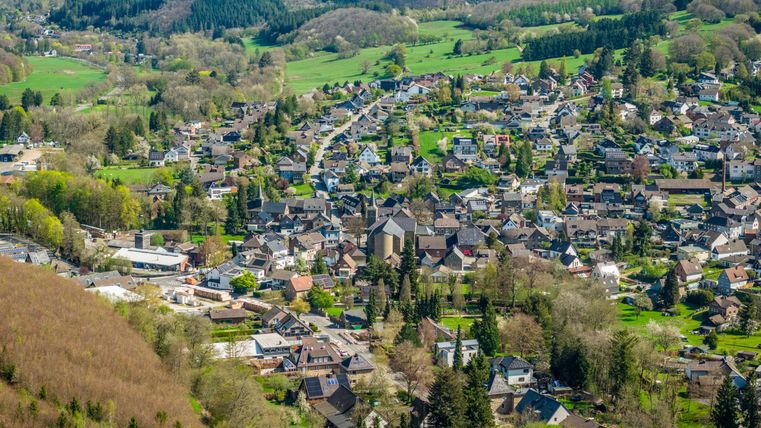 Une vue pittoresque d'un petit village avec de nombreuses maisons et des forêts verdoyantes dans les environs. Les douces collines et le paysage clair transmettent une sensation calme et idyllique.
