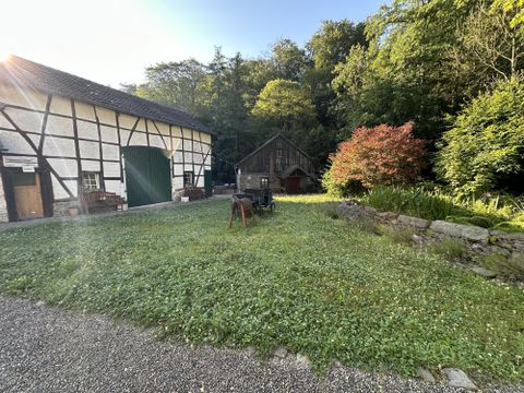 Ein idyllischer Hof mit einem alten Fachwerkhaus und einer gemütlichen Scheune. Der grüne Garten ist umgeben von Bäumen und Blumen.