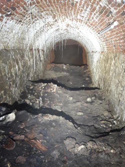 Ein dunkler Tunnel mit einem gewölbten Ziegeldach. Der Boden ist uneben und mit Müll und Schmutz bedeckt.