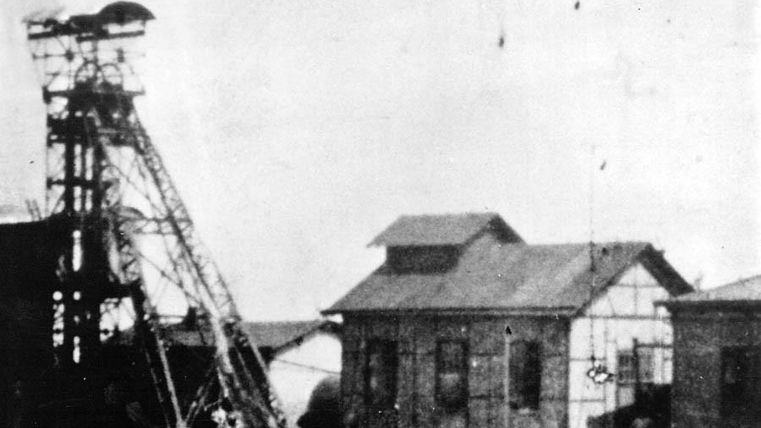 Ein historisches Industriegebäude mit einem Förderturm. Die Umgebung wirkt verlassen und zeigt Zeichen der Abnutzung.