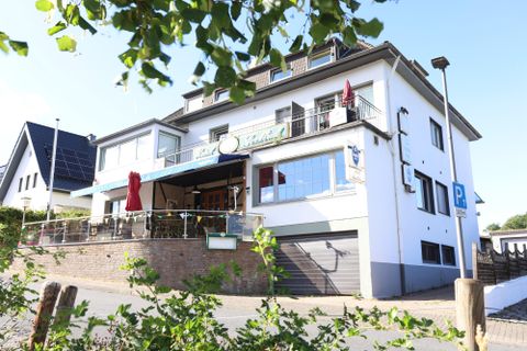 Ein modernes Gebäude mit einem gemütlichen Außenbereich. Die Fassade ist hell und freundlich, mit einem Parkplatz in der Nähe.