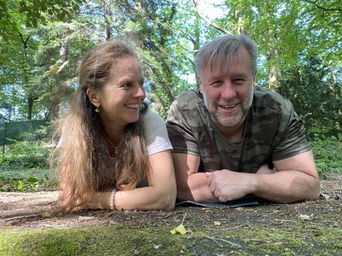 Ein Paar liegt entspannt im Wald auf dem Boden. Sie lächeln und genießen die Natur um sich herum.