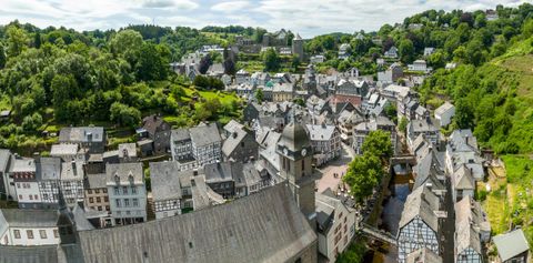 Eine malerische Stadt mit traditionellen Häusern und grünen Hügeln im Hintergrund. Der Himmel ist bewölkt und die Landschaft wirkt friedlich.