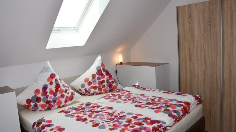Une chambre confortable avec un lit double et des coussins colorés. La pièce a un Velux et des meubles modernes en bois.