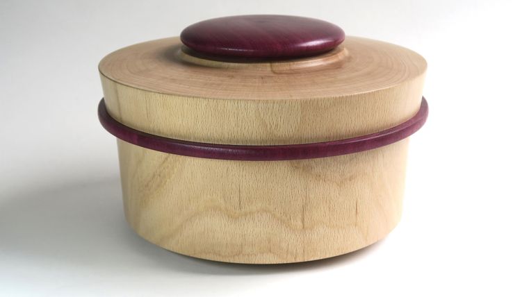 Eine wunderschöne Holzkiste mit einem runden Deckel. Die Kiste hat eine helle Farbe und einen lila Akzent.