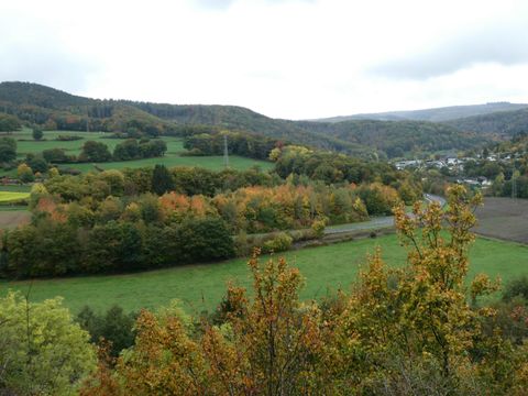 Eine malerische Landschaft mit sanften Hügeln und bunten Herbstbäumen. Im Hintergrund ist ein kleines Dorf zu sehen.