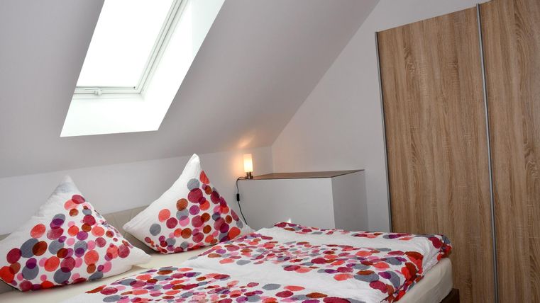 Une chambre confortable avec un lit double et des coussins colorés. Il y a une armoire et une lucarne qui laisse entrer la lumière du jour.