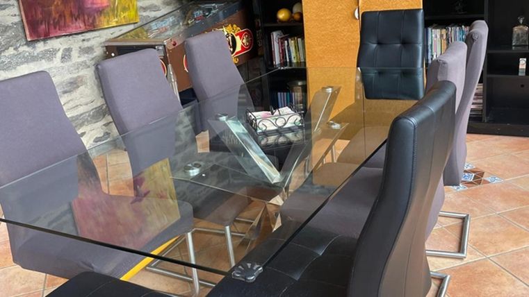 Een elegante eetruimte met een glazen tafel en zwarte stoelen. Op de achtergrond zijn boekenkasten en decoratieve elementen zichtbaar.