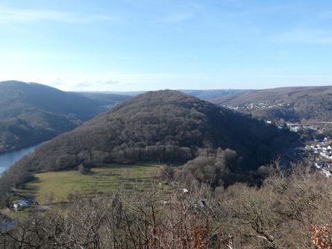 Eine malerische Hügellandschaft mit schneebedeckten Bäumen und einem ruhigen Fluss im Hintergrund. Der Himmel ist klar und blau.