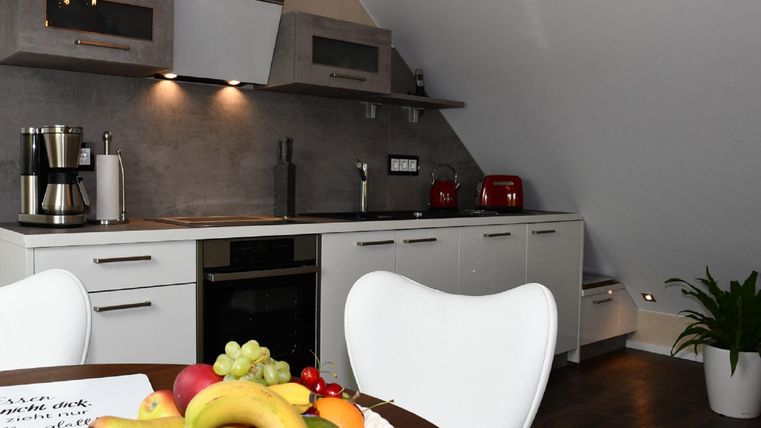 Une cuisine moderne avec des armoires blanches et un plan de travail élégant. Sur la table se trouve un bol de fruits avec différents fruits.