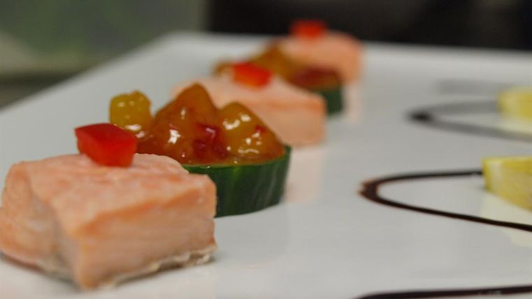 Ein Kunstwerk aus geräuchertem Lachs, serviert auf einem weißen Teller. Neben dem Lachs befinden sich bunte Saucen und frisches Gemüse.