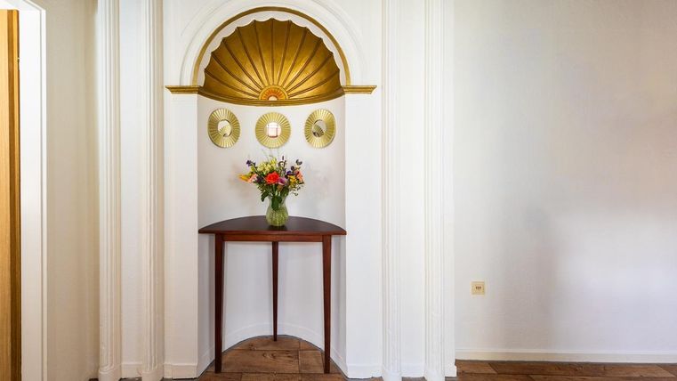 Ein eleganter Eingang mit einem runden Tisch und einer Blumenvase. An der Wand sind goldene Wanddekorationen zu sehen.