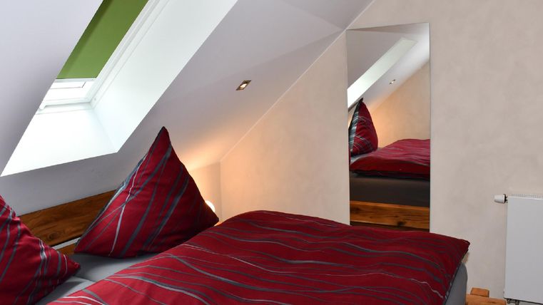 Une chambre de toit confortable avec un grand lit et des coussins colorés. Un miroir et une fenêtres de toit apportent de la lumière supplémentaire.