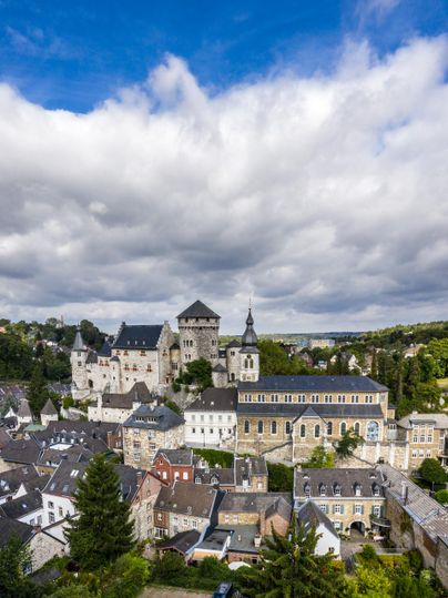 Eine schöne Stadtansicht mit historischen Gebäuden und einer Burg im Hintergrund. Der Himmel ist teils bewölkt und bietet einen weiten Blick über die Landschaft.
