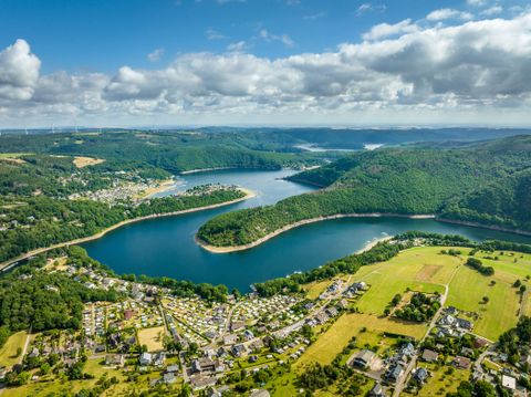 Ein weiter Blick über den Rursee mit Campingplätzen, Dörfern und Wäldern in hügeliger Umgebung.