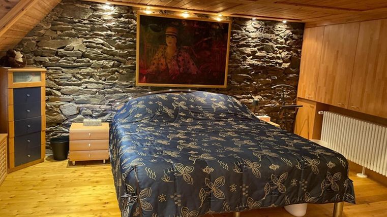 Een gezellige slaapkamer met een groot bed en een blauwe dekbedovertrek. De muren zijn bekleed met steen en hout, en er hangt een groot schilderij aan de muur.