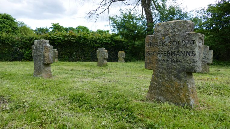 Un cimetière avec plusieurs pierres tombales dans un pré verdoyant. Les pierres tombales sont en pierre et portent l'inscription « Soldat inconnu ».
